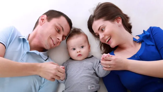 Mother and father looking at baby boy and holding his hands